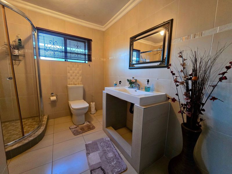 A functional bathroom featuring a tiled shower enclosure, a modern ceramic basin on a tiled vanity base, and neutral wall and floor tiling.