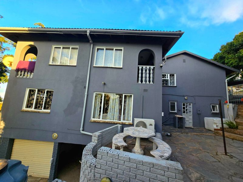 Rear exterior view of a multi-story house featuring a stone-paved patio, built-in stone seating, and balcony access with security bars on windows.