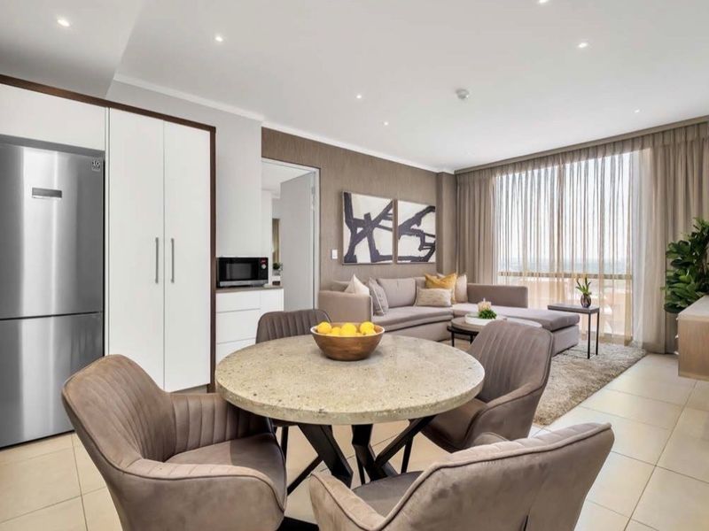 A modern open-plan living and dining area featuring tiled floors, recessed lighting, and seamless access to a balcony through large glass sliding doors.
