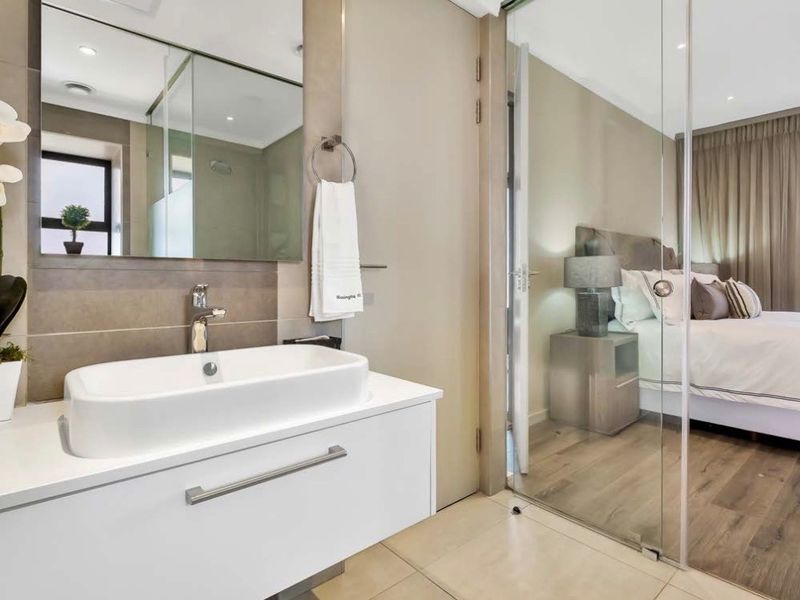 Modern bathroom featuring a sleek vanity with countertop basin, large wall mirror, and a glass partition separating the space from the adjacent bedroom.