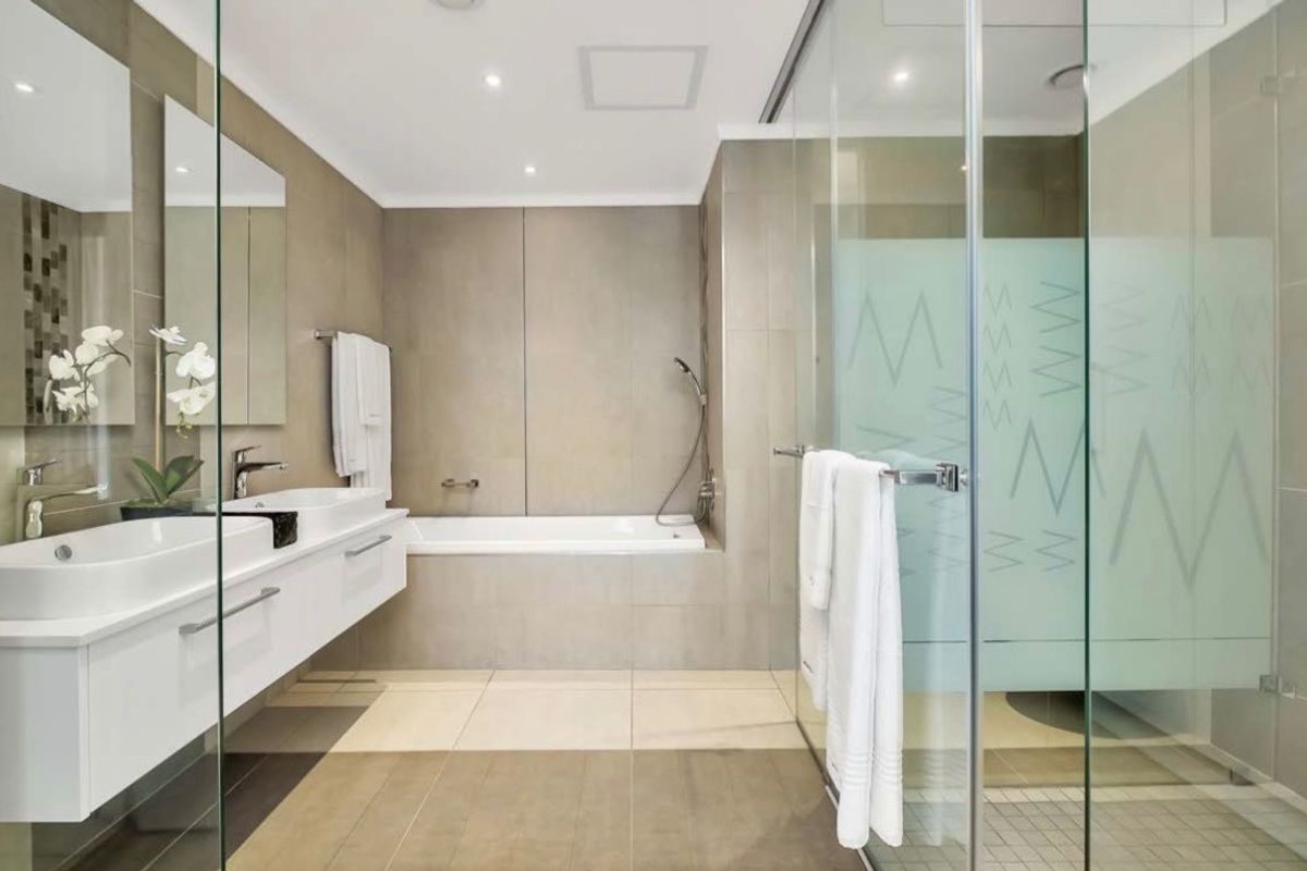 Modern bathroom featuring a double vanity with wall-mounted cabinetry, a built-in bathtub, and a spacious glass-enclosed shower with neutral tiling.