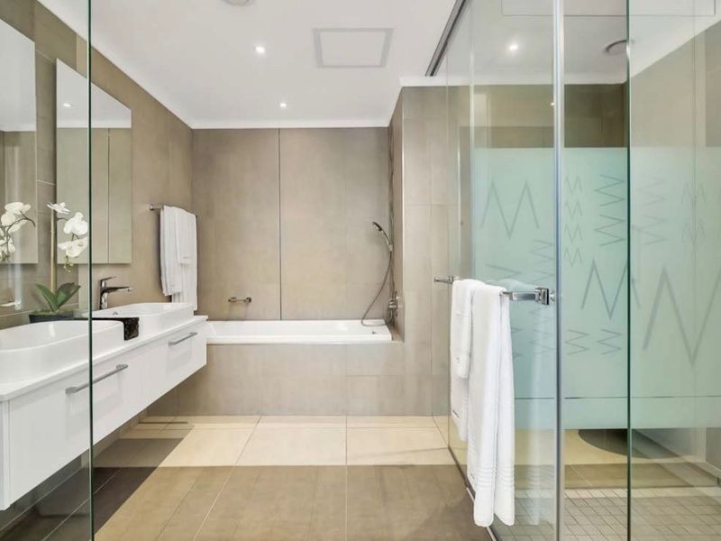 Modern bathroom featuring a double vanity with wall-mounted cabinetry, a built-in bathtub, and a spacious glass-enclosed shower with neutral tiling.
