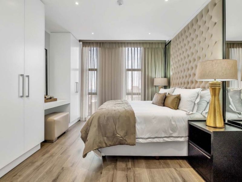 Modern bedroom featuring high-quality laminate flooring, extensive built-in cabinetry with integrated vanity, and a sophisticated upholstered feature wall.