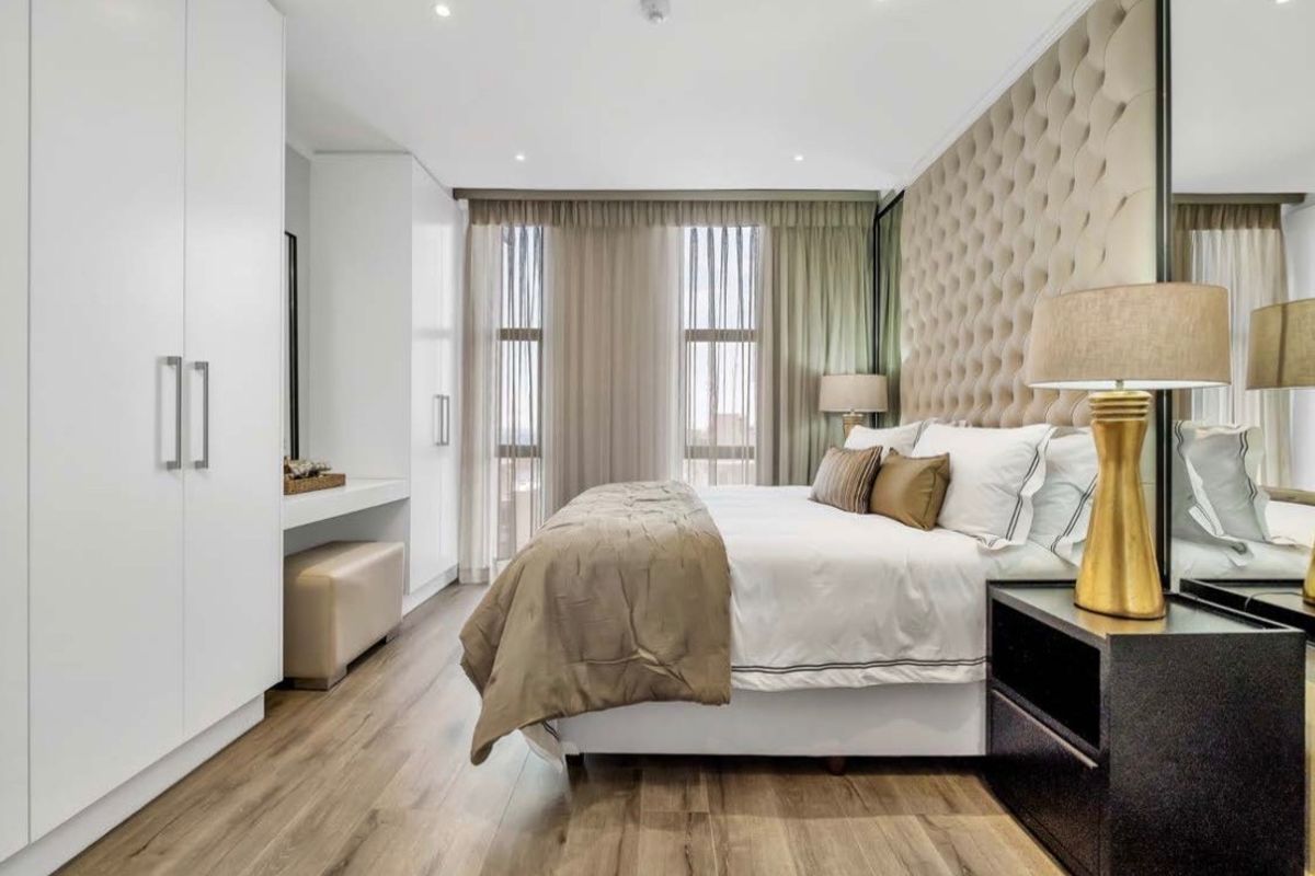 Modern bedroom featuring high-quality laminate flooring, extensive built-in cabinetry with integrated vanity, and a sophisticated upholstered feature wall.