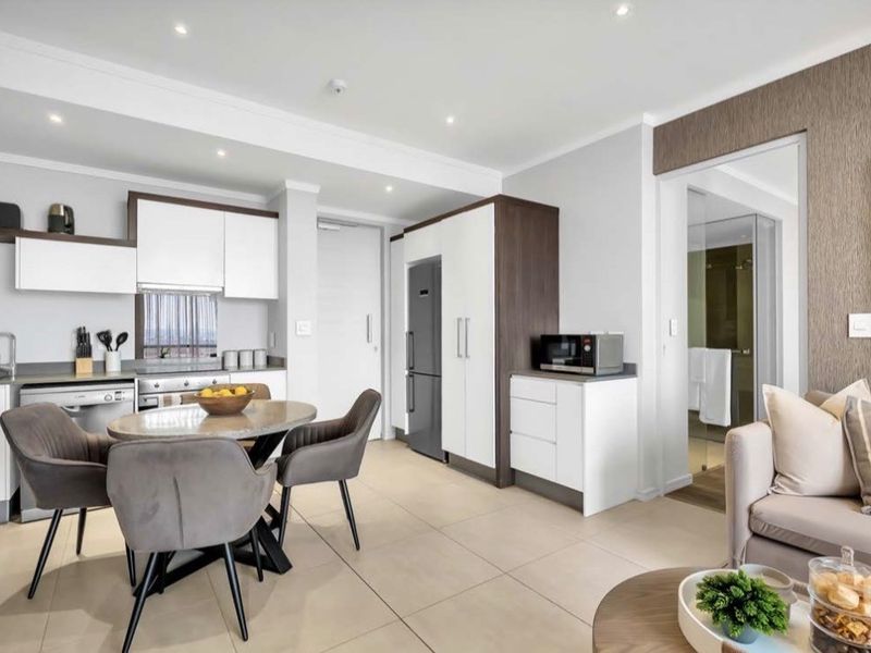 Modern open-plan kitchen and living area featuring sleek built-in cabinetry, integrated appliances, recessed lighting, and neutral tiled flooring.