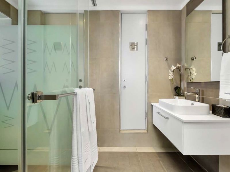 Modern bathroom featuring a wall-mounted vanity with a vessel sink, glass shower enclosure, and neutral tiled finishes.