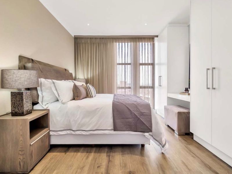 A modern, well-maintained bedroom featuring sleek built-in wardrobes, a integrated vanity area, recessed lighting, and high-quality laminate flooring.