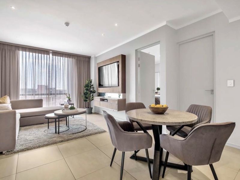 Modern open-plan living and dining area featuring neutral tiled flooring, recessed lighting, and a sleek built-in media console with large glass sliding doors.