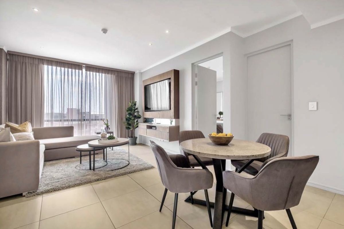 Modern open-plan living and dining area featuring neutral tiled flooring, recessed lighting, and a sleek built-in media console with large glass sliding doors.