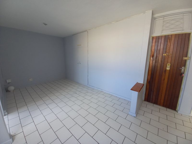 An empty entrance area featuring tiled flooring, built-in storage cupboards, and a solid timber front door with security gate.
