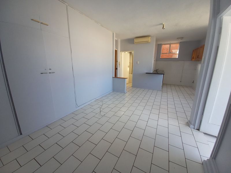 An open-plan living and kitchen area featuring tiled flooring, built-in storage cupboards, and a compact kitchen layout with basic cabinetry.