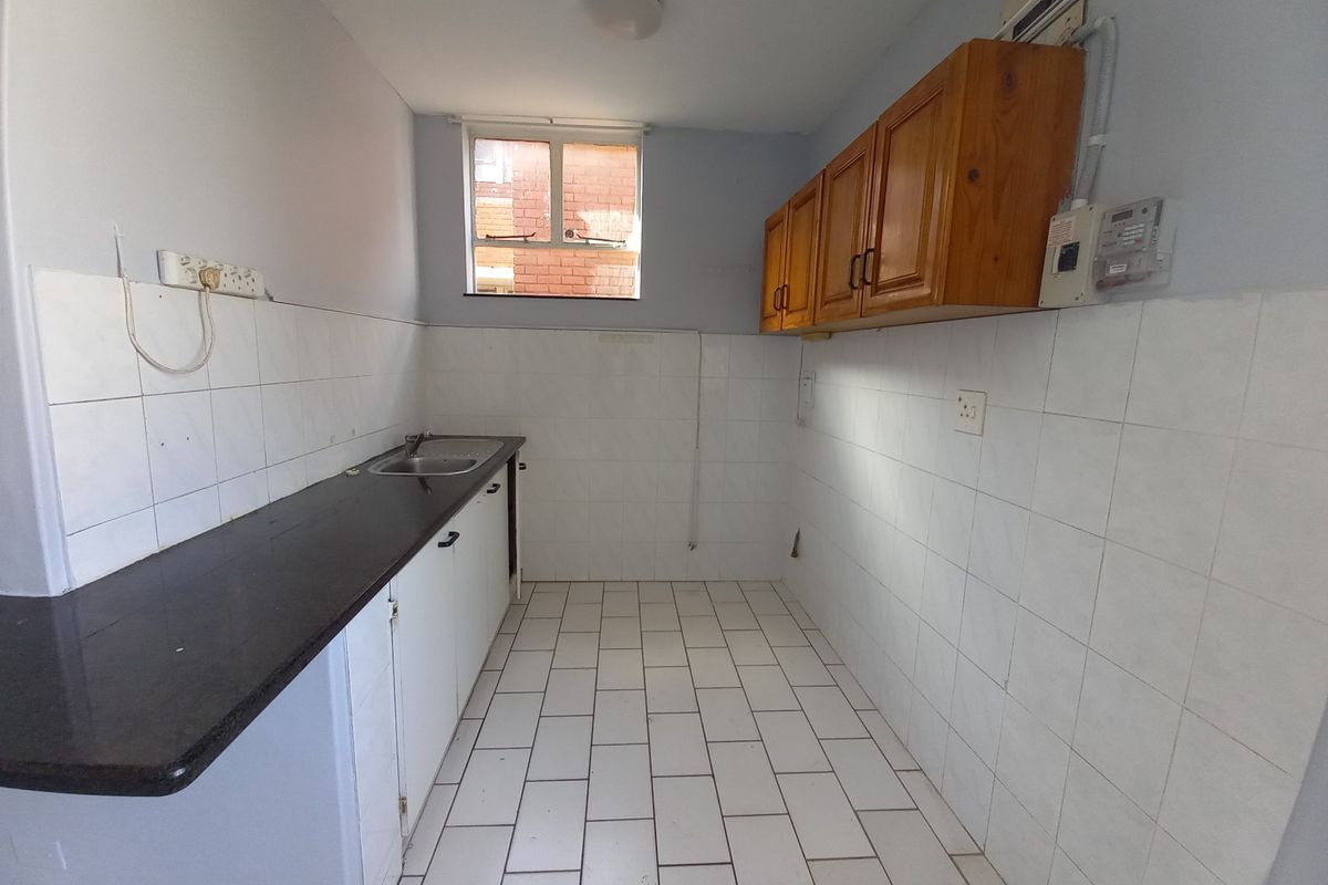 A functional, empty kitchen featuring tiled flooring, built-in cabinetry, a laminate countertop, and a stainless steel sink, ready for modernization.