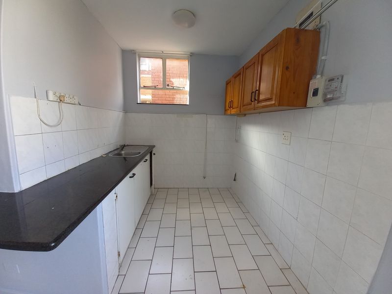 A functional, empty kitchen featuring tiled flooring, built-in cabinetry, a laminate countertop, and a stainless steel sink, ready for modernization.