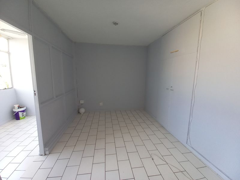 An empty bedroom featuring tiled flooring, built-in cupboards, and decorative wainscoting on the wall, offering a clean and neutral space ready for personalization.