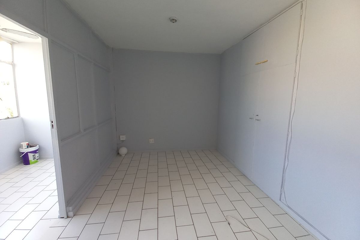 An empty bedroom featuring tiled flooring, built-in cupboards, and decorative wainscoting on the wall, offering a clean and neutral space ready for personalization.
