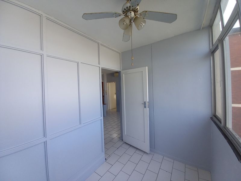 An enclosed balcony or sunroom featuring tiled flooring, a ceiling fan, and large windows, providing a bright and versatile additional living space.