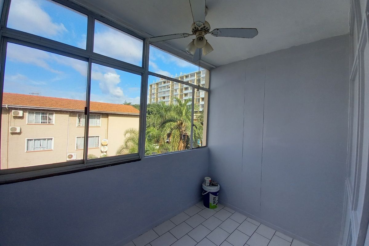 An enclosed balcony featuring tiled flooring, a ceiling fan, and large windows offering an urban view, suitable for a sunroom or study area.