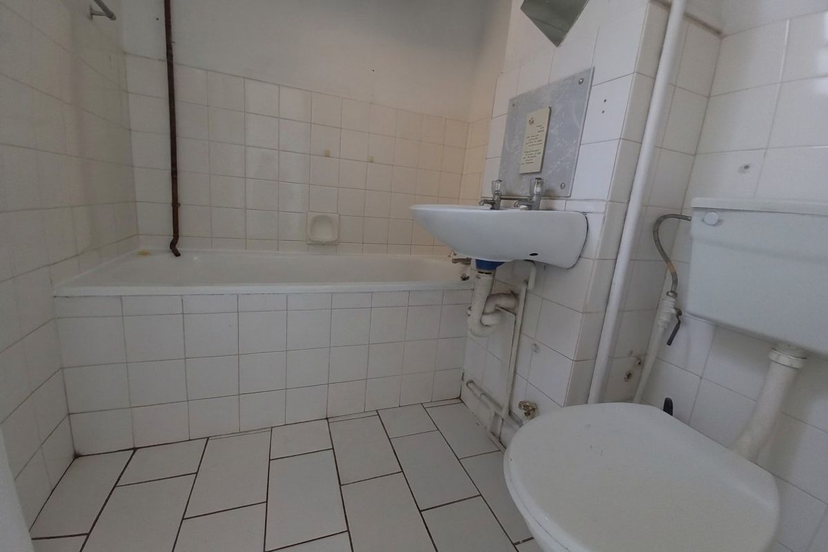 A dated bathroom featuring a standard bathtub, wall-mounted basin, and toilet with exposed plumbing and white tiled finishes throughout.