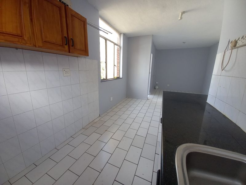 An empty kitchen featuring wooden cabinetry, a granite countertop with an integrated sink, and tiled flooring, offering a functional space ready for updates.