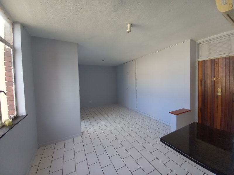 An empty open-plan living area featuring tiled flooring, built-in storage, and a granite breakfast counter, offering a blank canvas for interior design.