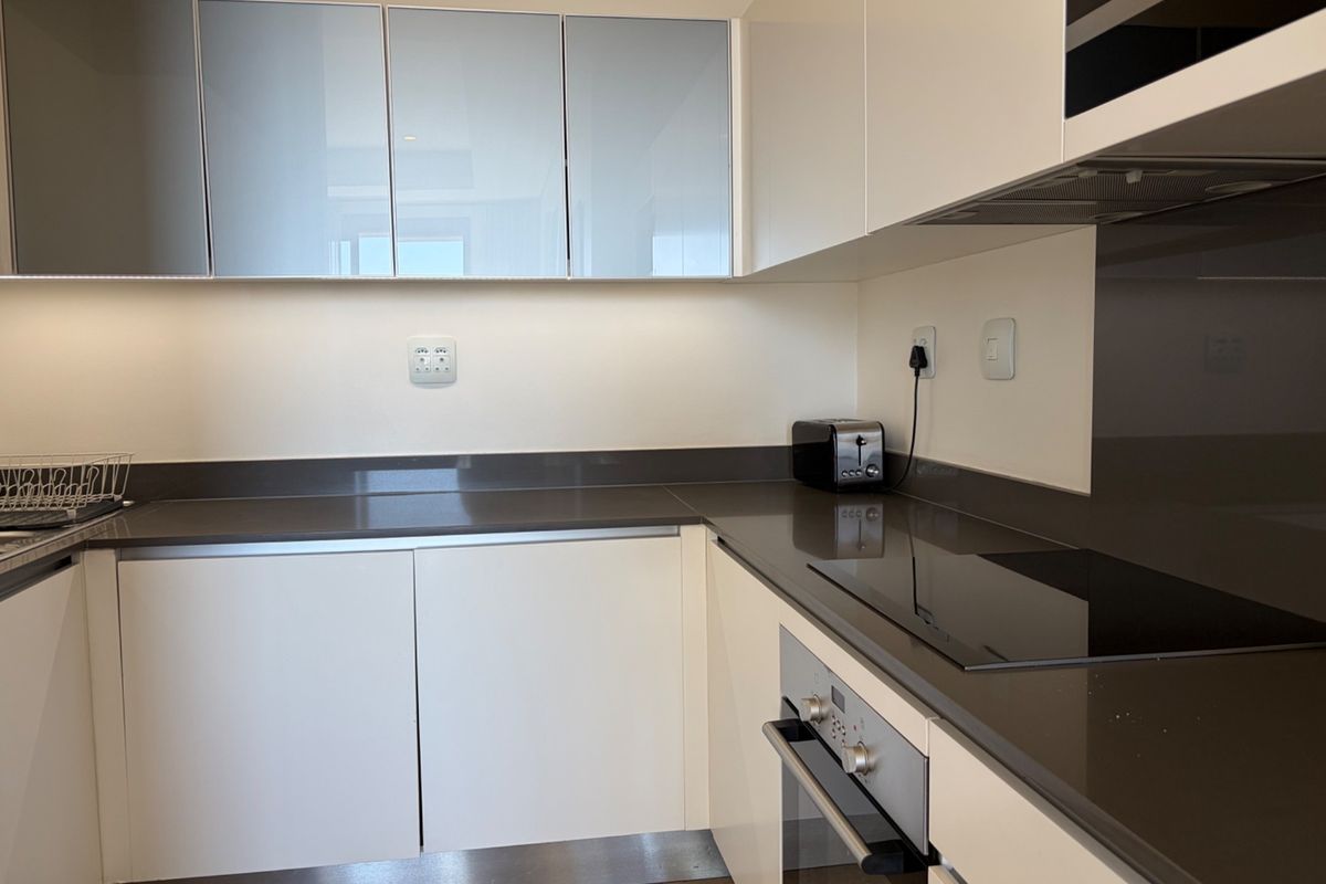 Modern kitchen featuring sleek white cabinetry, dark stone countertops, integrated appliances including an oven, hob, and microwave, and a glass splashback.