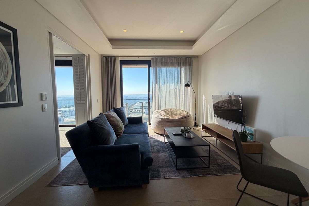 A bright and modern living room featuring tiled floors, a recessed ceiling with downlights, and a large sliding glass door leading to a balcony.
