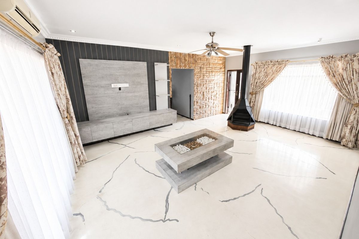 Spacious living room featuring a modern freestanding fireplace, stone accent wall, built-in media cabinetry, and polished flooring with decorative inlay.