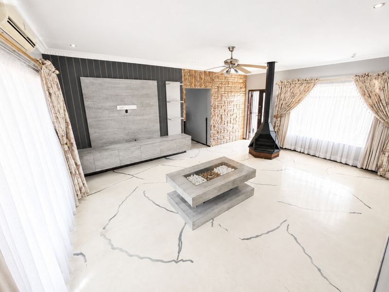 Spacious living room featuring a modern freestanding fireplace, stone accent wall, built-in media cabinetry, and polished flooring with decorative inlay.