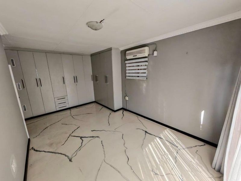 A spacious bedroom featuring extensive built-in cabinetry, an air conditioning unit, and unique marble-effect flooring.