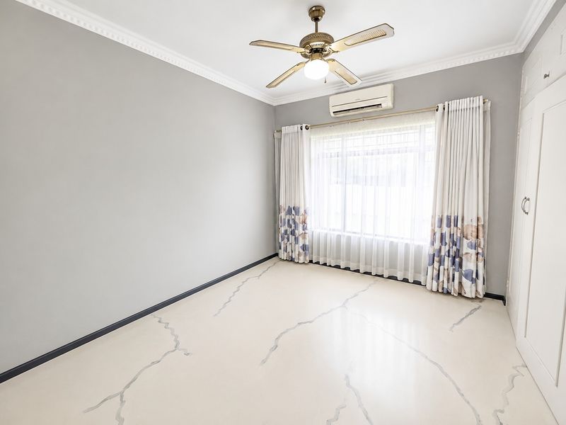 A bright, empty bedroom featuring tiled flooring, crown molding, a ceiling fan, and a built-in wardrobe with an integrated air conditioning unit.