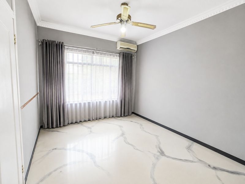 A bright, empty bedroom featuring marble-look tile flooring, crown molding, a ceiling fan, and a wall-mounted split system air conditioner.