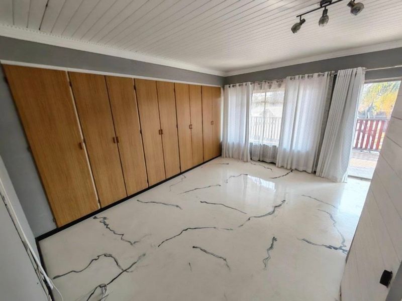 A bright bedroom featuring extensive built-in wooden cupboards, unique marble-effect flooring, and direct access to an outdoor area through a sliding door.