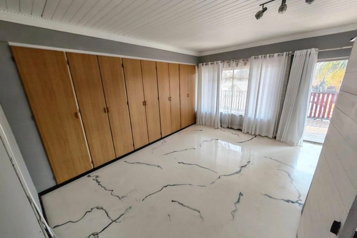 A bright bedroom featuring extensive built-in wooden cupboards, unique marble-effect flooring, and direct access to an outdoor area through a sliding door.