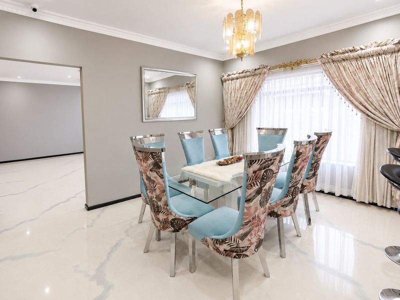 Elegant dining room featuring polished marble-look tiled flooring, decorative crown molding, and a sophisticated chandelier, creating a bright and refined atmosphere.