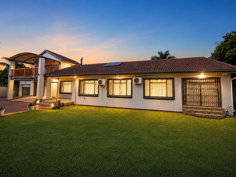 Rear view of the property featuring a spacious lawn, a covered balcony, and well-maintained exterior finishes with integrated security features.