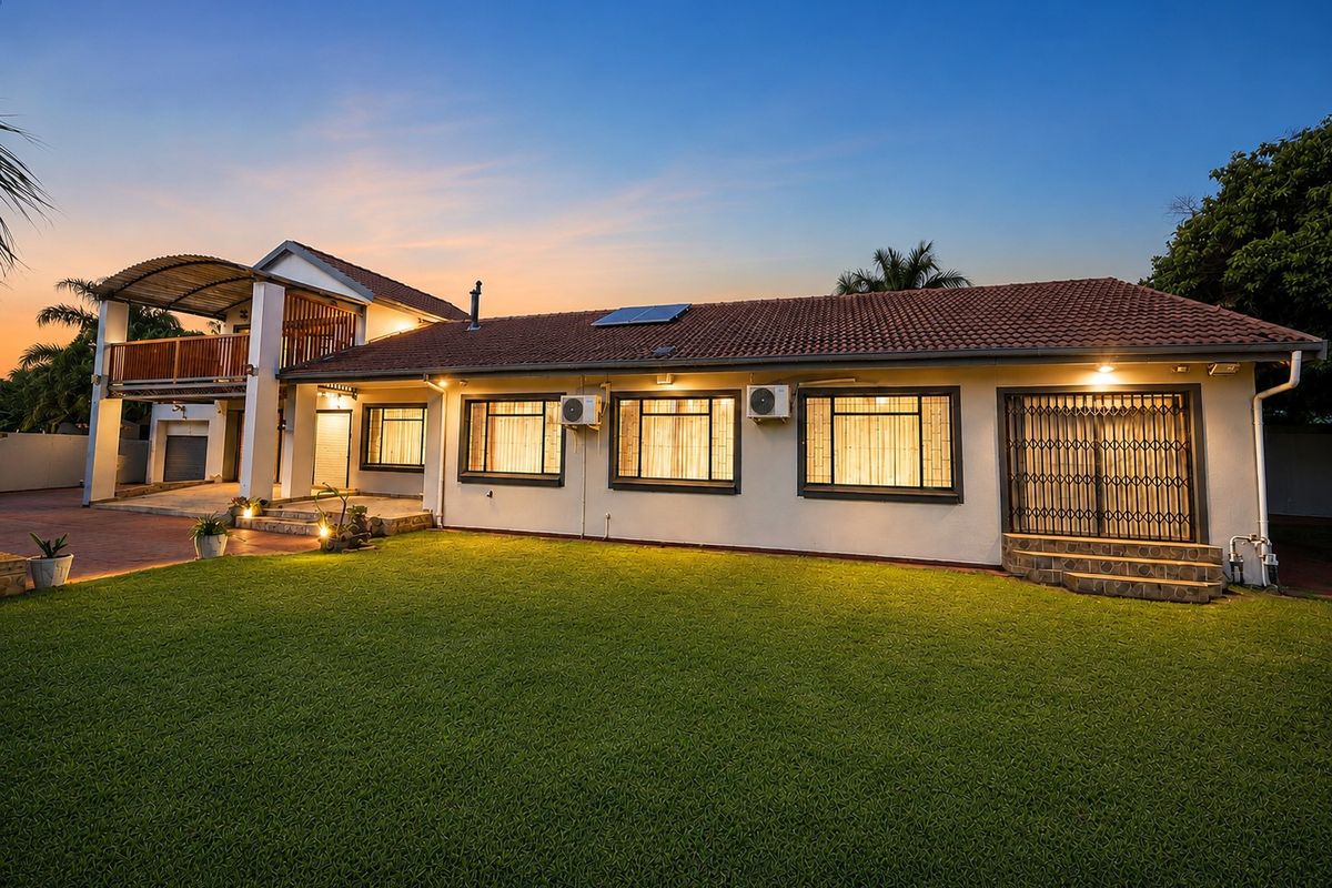 Rear view of the property featuring a spacious lawn, a covered balcony, and well-maintained exterior finishes with integrated security features.