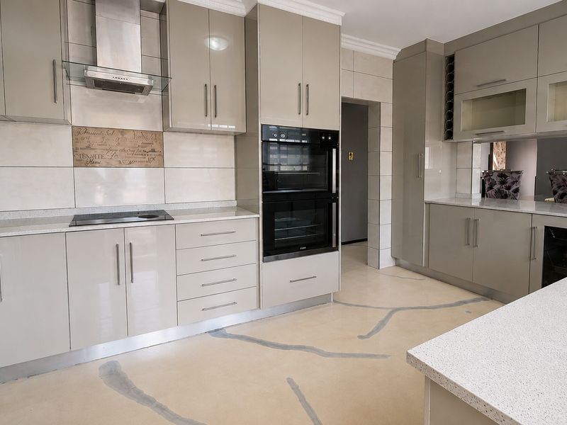 Modern kitchen featuring high-gloss cabinetry, quartz countertops, integrated double wall oven, electric hob, and a stylish tiled backsplash.