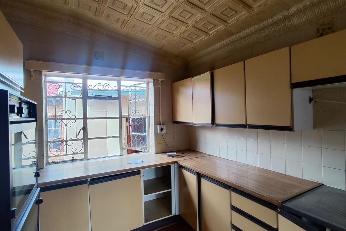 A dated kitchen featuring original cabinetry, laminate countertops, and decorative ceiling tiles, offering significant potential for a modern renovation.