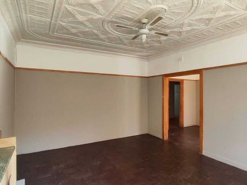 Spacious living area featuring a decorative pressed metal ceiling, ceiling fan, timber picture rails, and original parquet flooring.