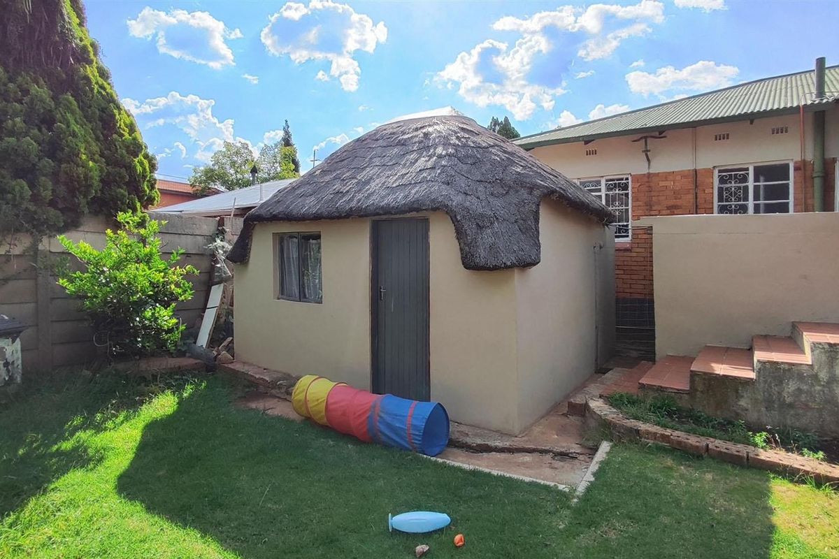A rear garden view featuring a small outbuilding with a traditional thatch roof, set against a brick boundary wall and landscaped lawn.