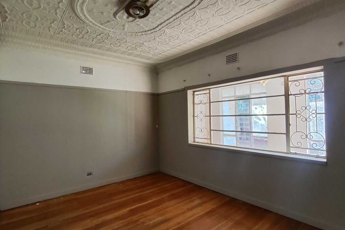 Spacious bedroom featuring original ornate pressed metal ceilings, polished timber flooring, and built-in storage with secure window bars.