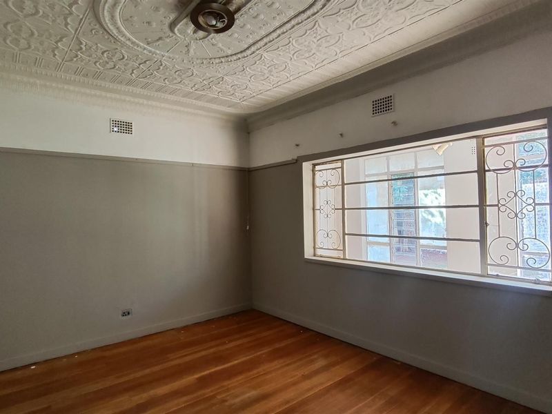 Spacious bedroom featuring original ornate pressed metal ceilings, polished timber flooring, and built-in storage with secure window bars.