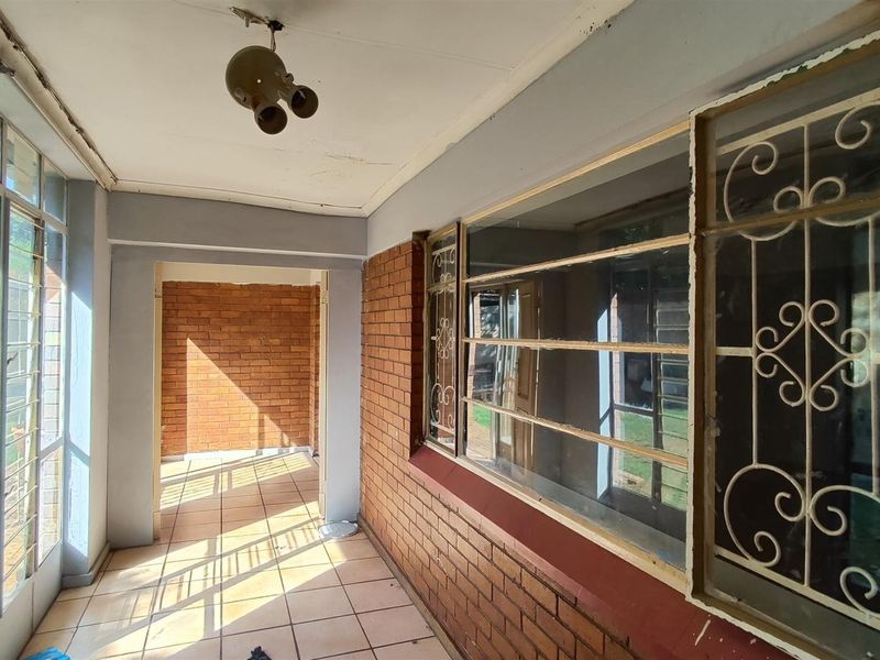 A covered patio area featuring exposed brick walls, tiled flooring, and metal security bars on the windows.