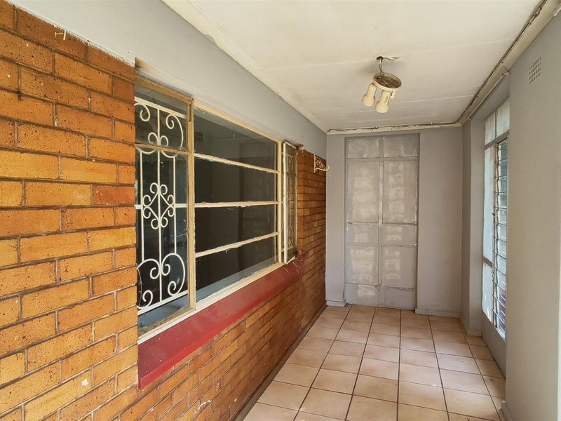 A covered patio area featuring exposed brick walls, tiled flooring, and security bars on the windows, offering a functional outdoor transition space.