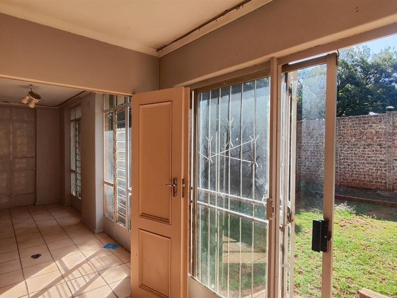An empty living area featuring tiled flooring and sliding glass doors that open directly onto a private garden with a brick boundary wall.