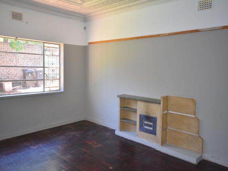 Empty living room featuring original parquet flooring, ornate ceiling detailing, and a built-in fireplace with integrated shelving.