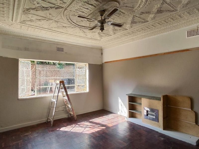 Spacious living room featuring original ornate pressed metal ceilings, parquet flooring, and a built-in fireplace, currently undergoing renovation with unfinished wall surfaces.