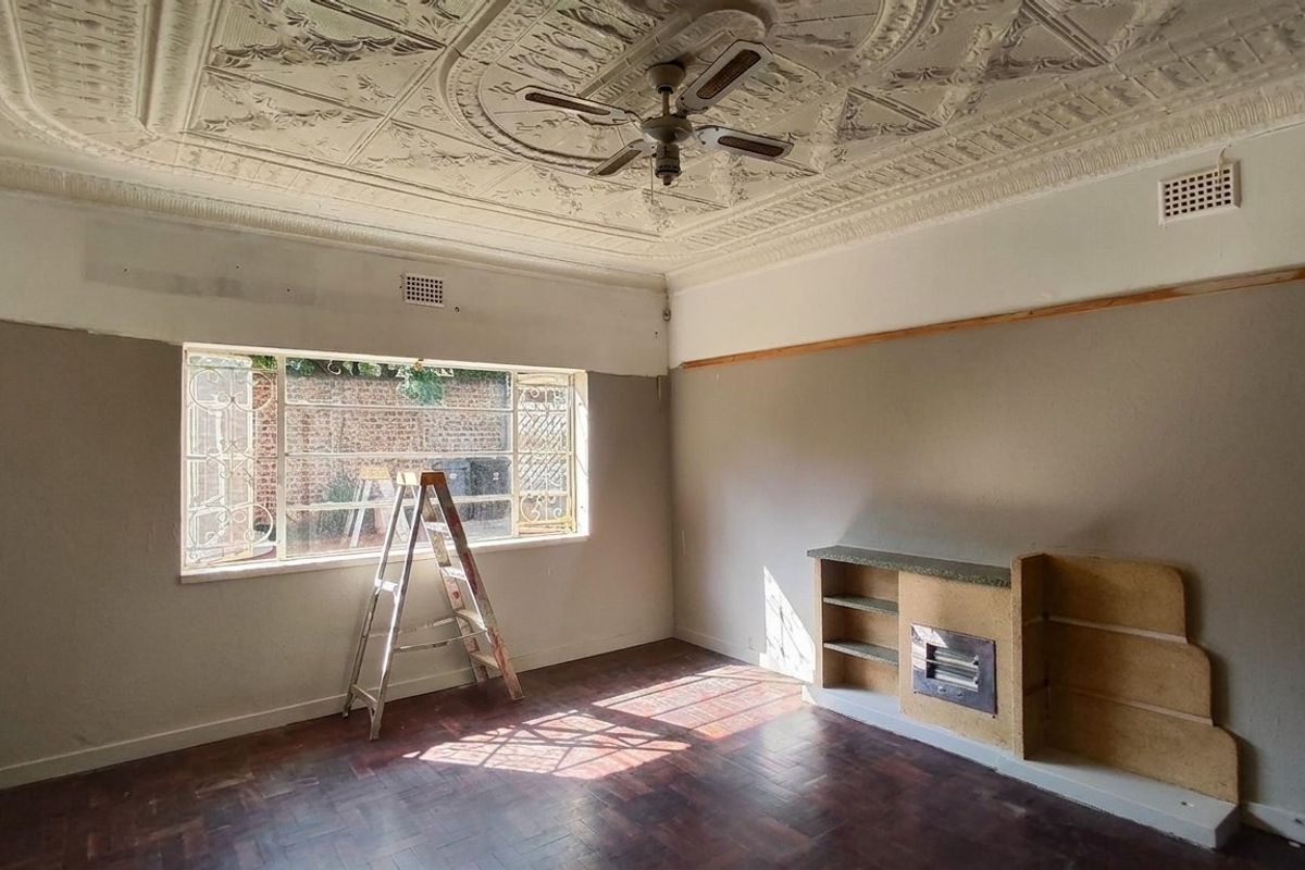 Spacious living room featuring original ornate pressed metal ceilings, parquet flooring, and a built-in fireplace, currently undergoing renovation with unfinished wall surfaces.