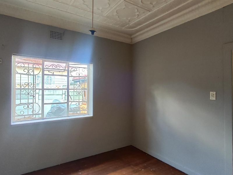 An empty living room featuring original pressed metal ceilings, ornate cornices, and timber flooring, with a view through to the kitchen area.
