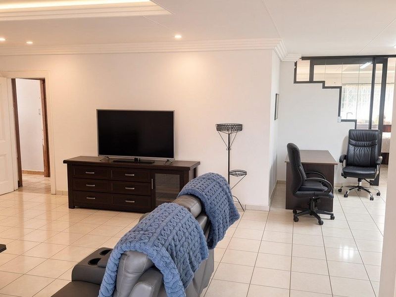 Spacious living area featuring neutral tiled flooring, recessed ceiling lighting, and coved cornicing, providing a versatile open-plan layout.